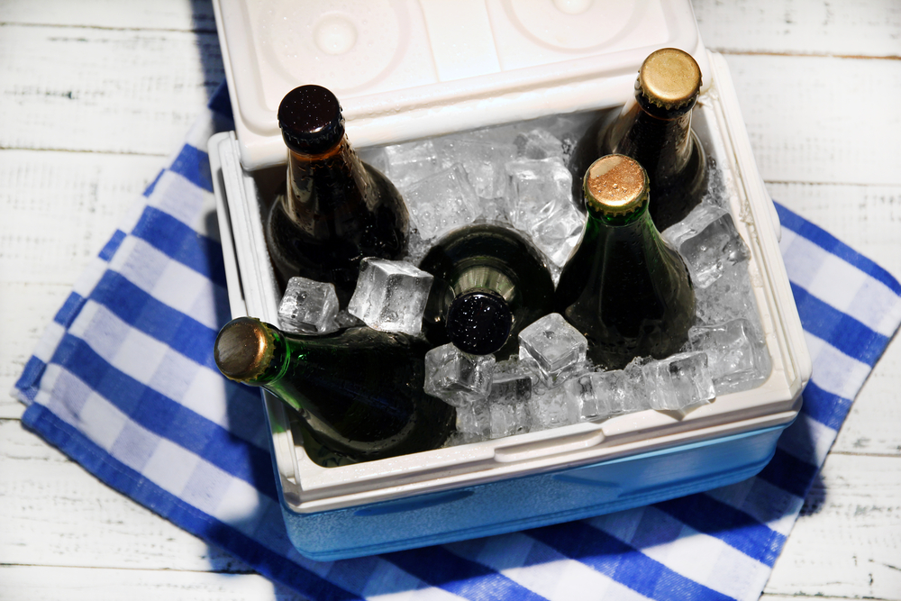 Ice chest full of drinks in bottles on color napkin, on wooden background - stock photo